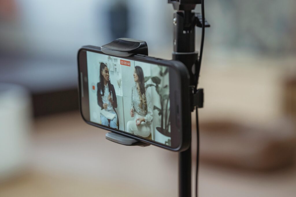 Due ragazze riprese dalla telecamera di uno smartphone mentre registrano contenuti video, evidenziando creatività e interazione con il pubblico.
